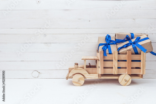 Wooden toy truck with gift boxes in the back on a white wooden b