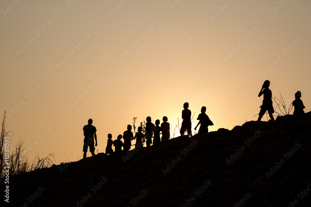 silhouette row of children walking along with young man in the wonderful orange sunset