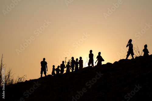 silhouette row of children walking along with young man in the wonderful orange sunset