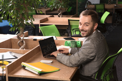 Portrait of happy businessman working in office. Hnadsome man sitting at working place and using laptop computer for business purposes. photo