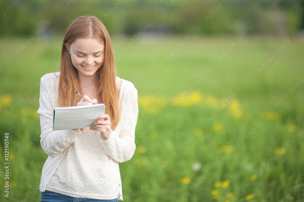 Happy Girl European appearance standing on the grass with notebook and pen Happy Girl European appearance standing on the grass with notebook and pen