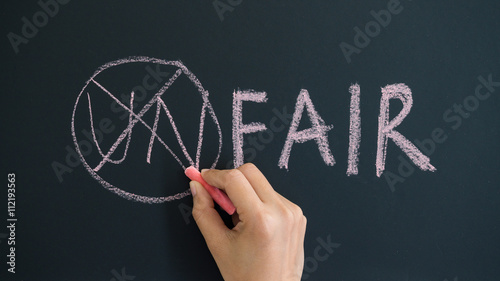 Fotografi Hand using chalk changing the word unfair to fair by crossing the word un on the