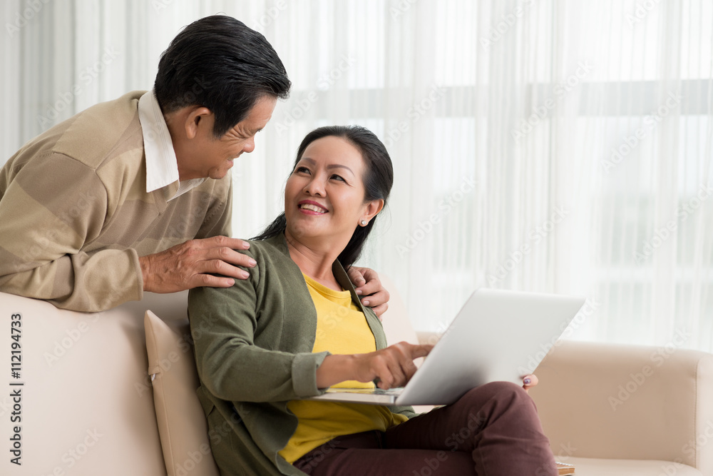 Smiling mature woman discussing something on laptop with her husband Smiling mature woman discussing something on laptop with her husband