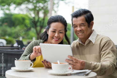 Smiling aged couple reading news on tablet computer