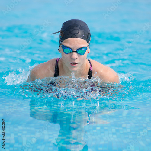 Young girl in goggles and cap swimming butterfly stroke style in the blue water pool