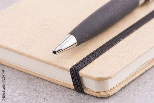 Notepad and pen lying on office desk in close up. Brown notebook and black pen. Concept of business meeting, taking notes or education.