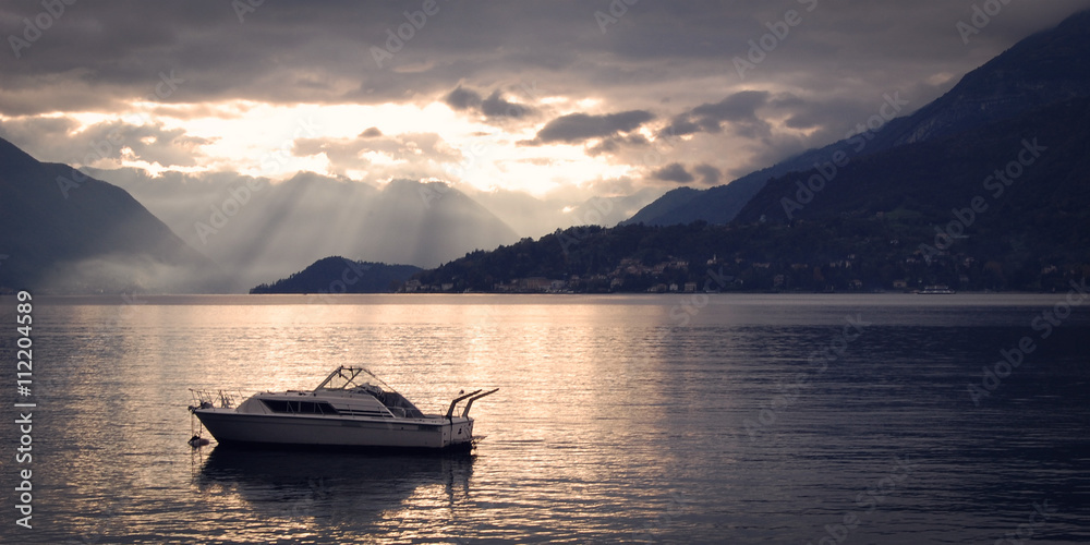Boat on Lake Como at the sunset. Silver linings in Lake Como at the sunset. Retro style photo. Sunset view of the lake in Lombardy. Varenna, Lake Como, Italy.