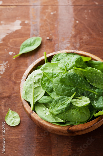 Baby spinach leaves in wooden bowl on old rustic table, organic food