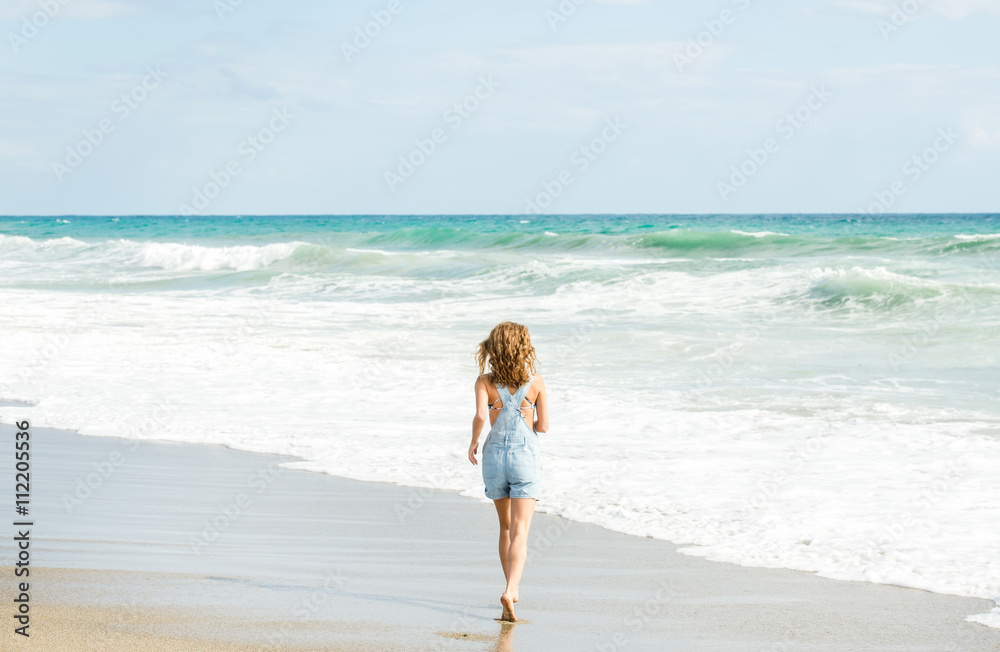 Young woman in blue denim jumpsuit walking to the sea