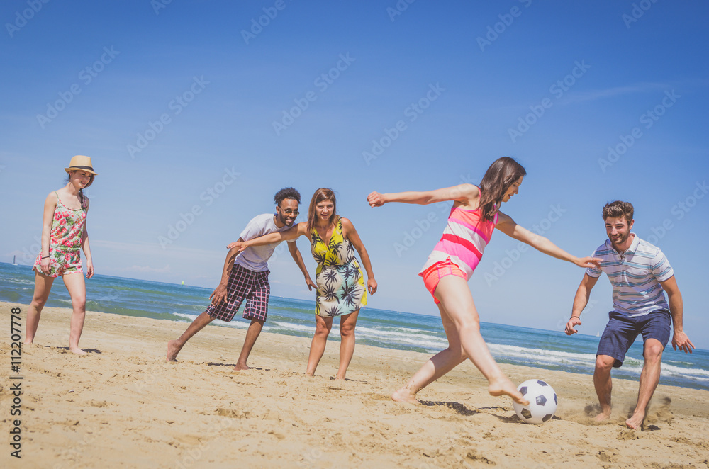 Group of multiracial friends playing football at the beach
