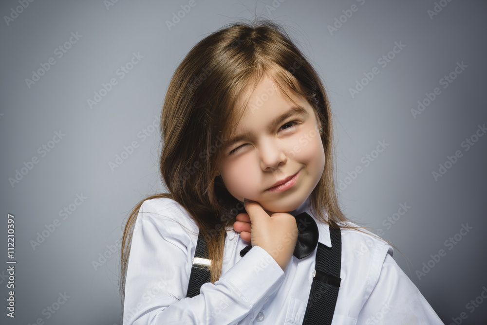 Portrait of cute girl winking over gray background. Looking at the camera. Positive human emotion facial expression body language Portrait of cute girl winking over gray background. Looking at the camera. Positive human emotion facial expression body language