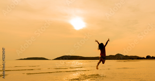 Silhouette of little asian girls jumping on beach in sunset time
