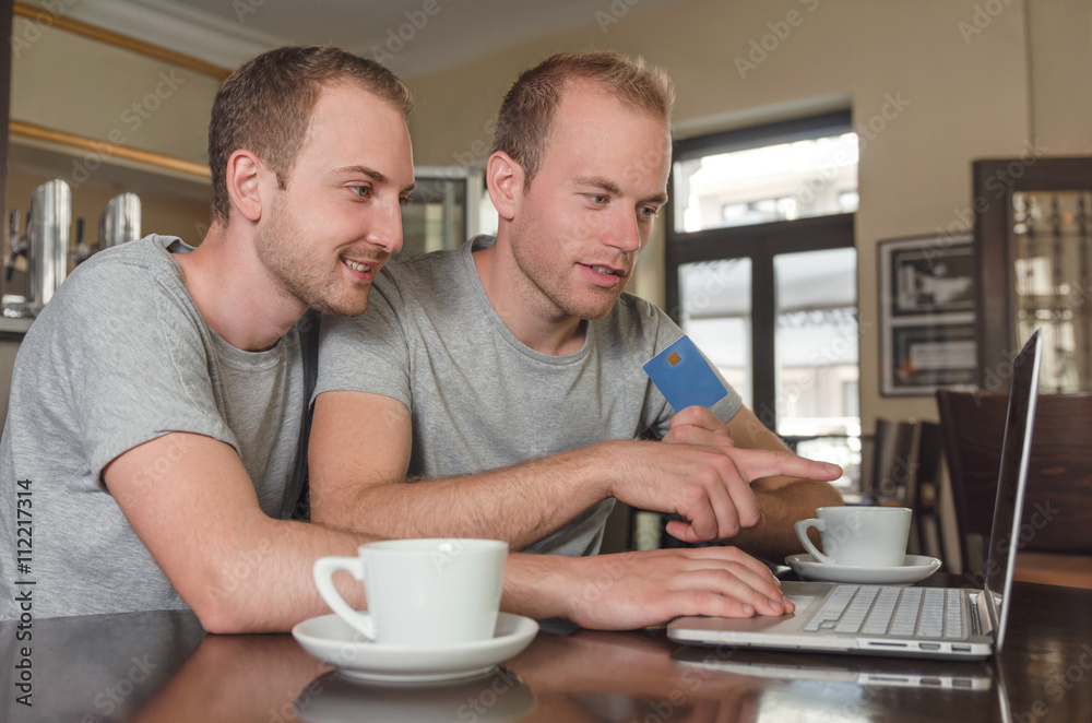 smiling gay couple doing online banking on their laptop smiling gay couple doing online banking on their laptop