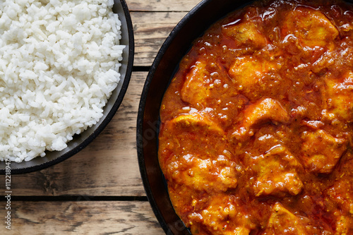 Chicken tikka masala traditional meat curry spicy food with rice in cast iron skillet on vintage wooden background