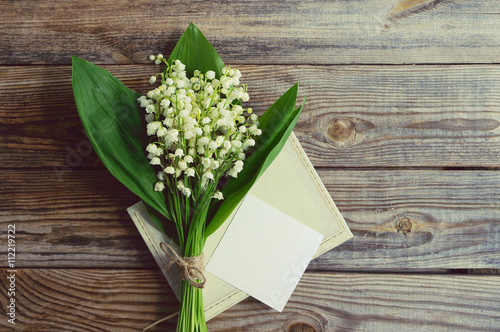 Bouquet of lilies of the valley, notebook and the empty white card for an inscription on a wooden background. Romantic bouquet with spring lilies of the valley