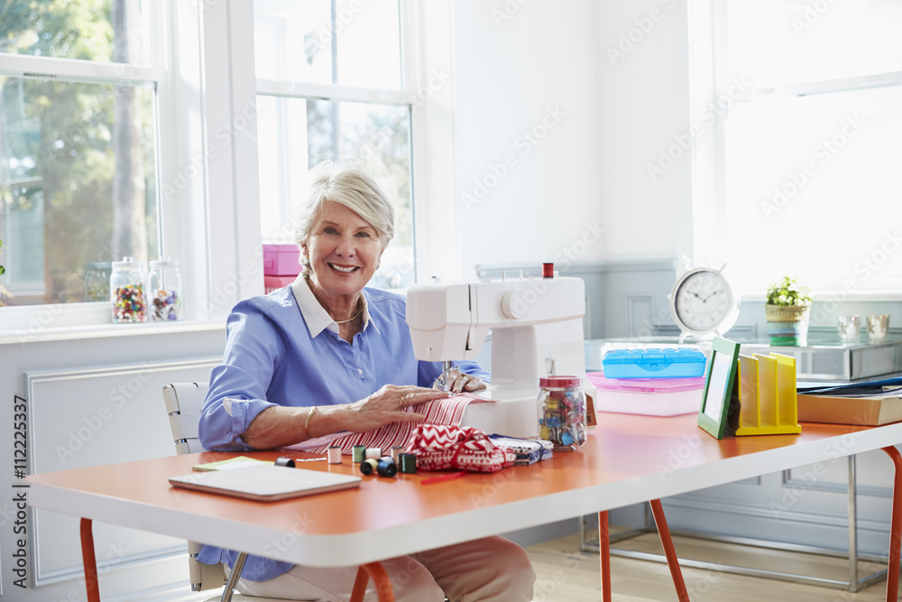 Senior Woman Making Clothes Using Sewing Machine At Home