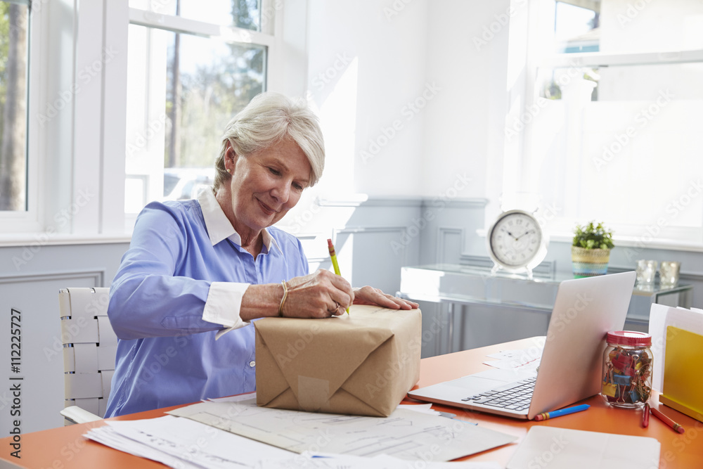 Senior Woman At Home Addressing Package For Mailing
