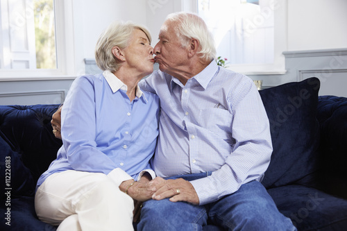 Affectionate Senior Couple Sitting On Sofa At Home