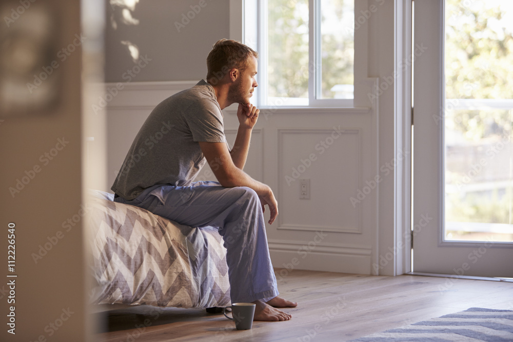Man Wearing Pajamas Sitting On Bed With Hot Drink Man Wearing Pajamas Sitting On Bed With Hot Drink