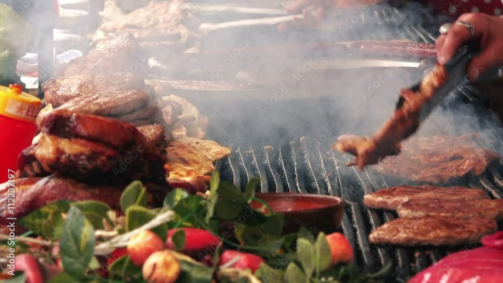 Barbecue on traditional outdoor festival, people preparing chicken and pork meat on a grill.