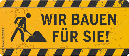 gelbes Schild Wir bauen für Sie mit Bauarbeiter-Icon zerkratzt
