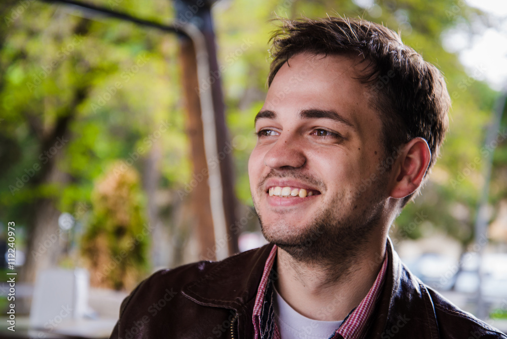 Positive young man alone behind table in summer cafe smiling looking sideways Positive young man alone behind table in summer cafe smiling looking sideways