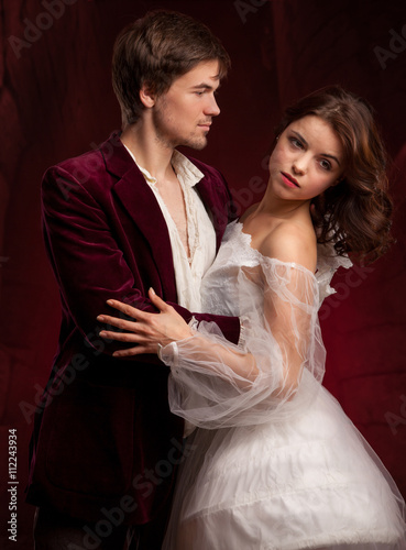 Portrait of young couple in love posing at studio dressed in classic clothes