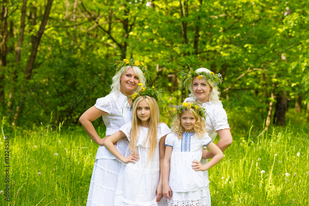 Fototapeta premium Happy family resting on the nature in the summer. Mom and daughter with wreath in the flowers in the park