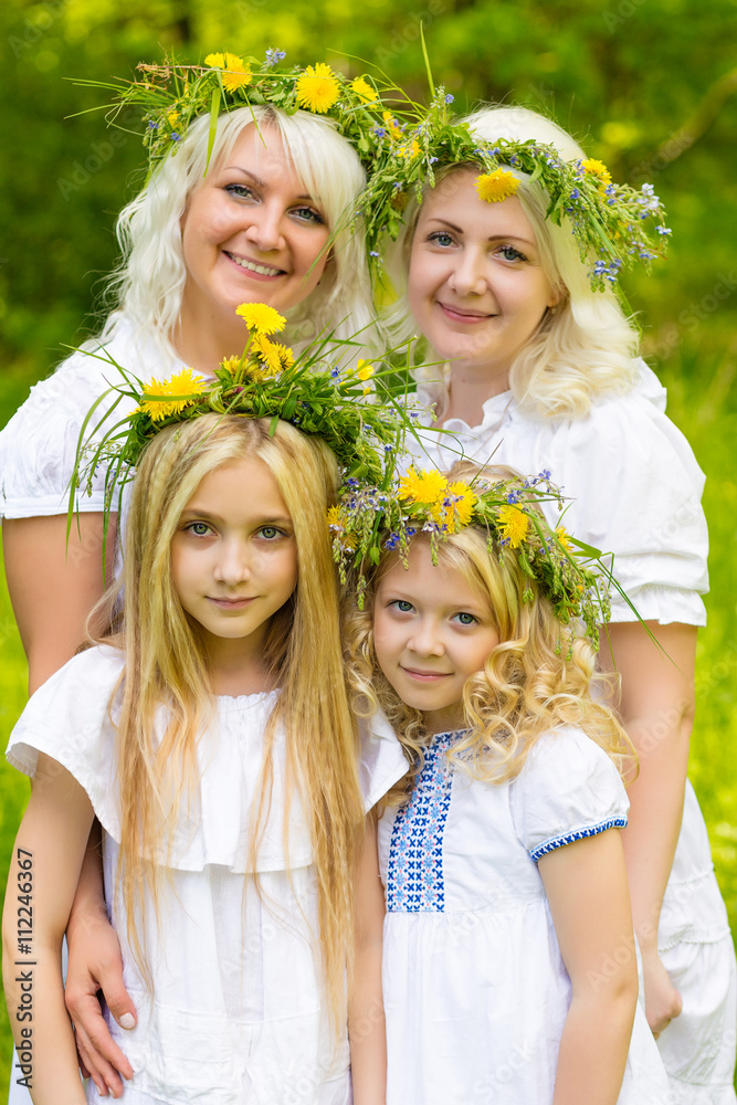 Happy family resting on the nature in the summer. Mom and daughter with wreath in the flowers in the park Happy family resting on the nature in the summer. Mom and daughter with wreath in the flowers in the park