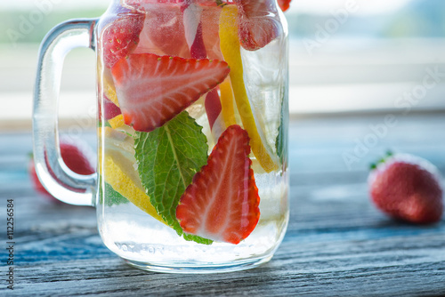 Jug with lemon and strawberry infused water on a rustic wooden surface
