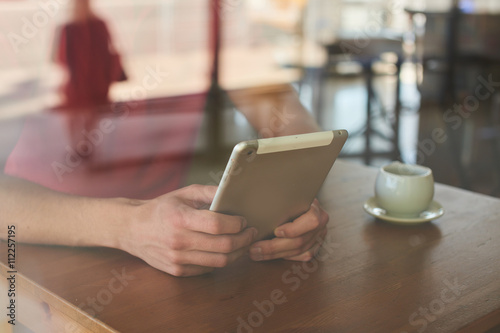 Hands holding the tablet while lying on a wooden table in cafe