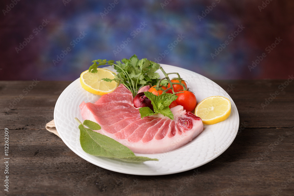 tuna steak raw on white plate with herbs and lemon