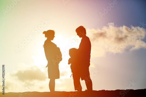 happy pregnant mother and father with son at sunset