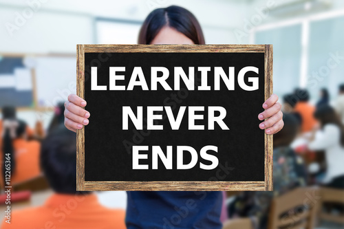 LEARNING NEVER ENDS message on the blackboard wooden frame on hand woman with blurred student study learning in classroom.