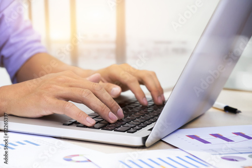 Businessman's hands typing on laptop keyboard and analyze marketing chart. © ijeab