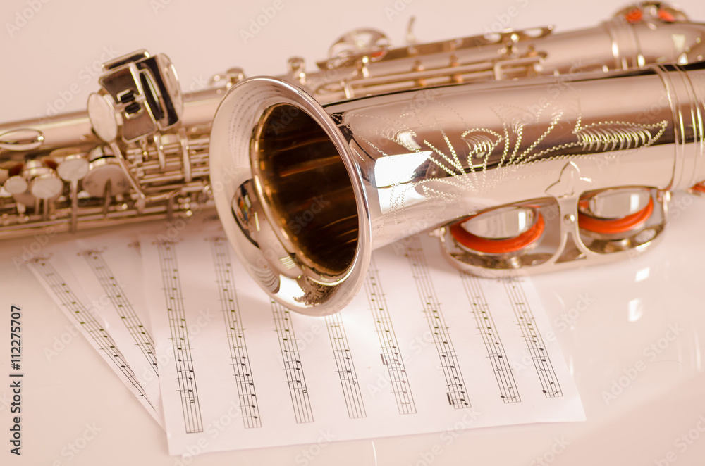 Naklejka premium Closeup partly view of shiny saxophone lying on musical notes paper