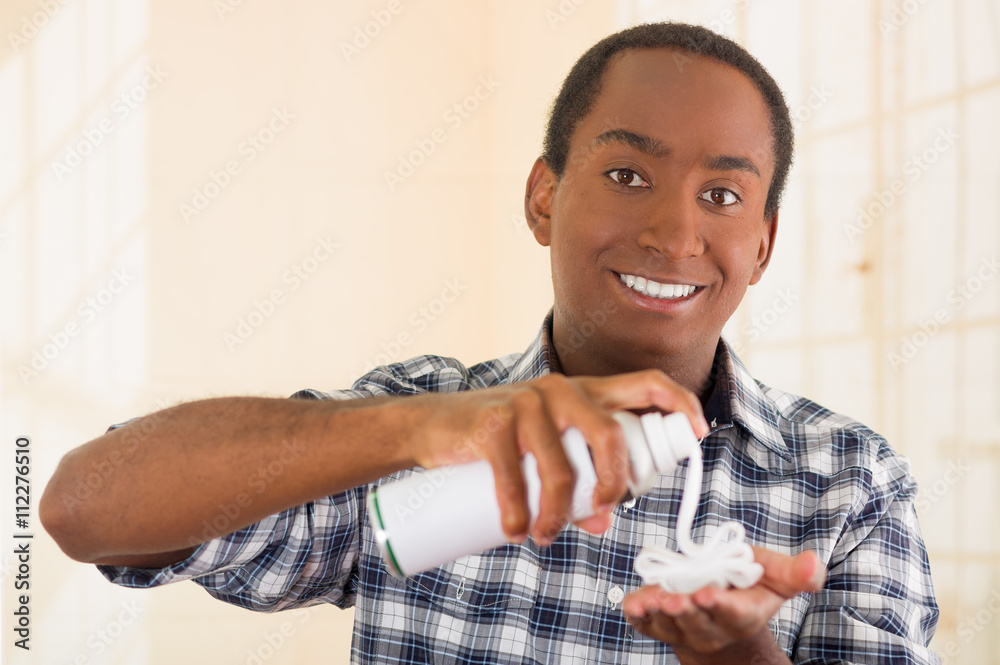 Handsome young man wearing white blue square pattern shirt squeezing shaving foam pile in left hand, smiling to camera Handsome young man wearing white blue square pattern shirt squeezing shaving foam pile in left hand, smiling to camera
