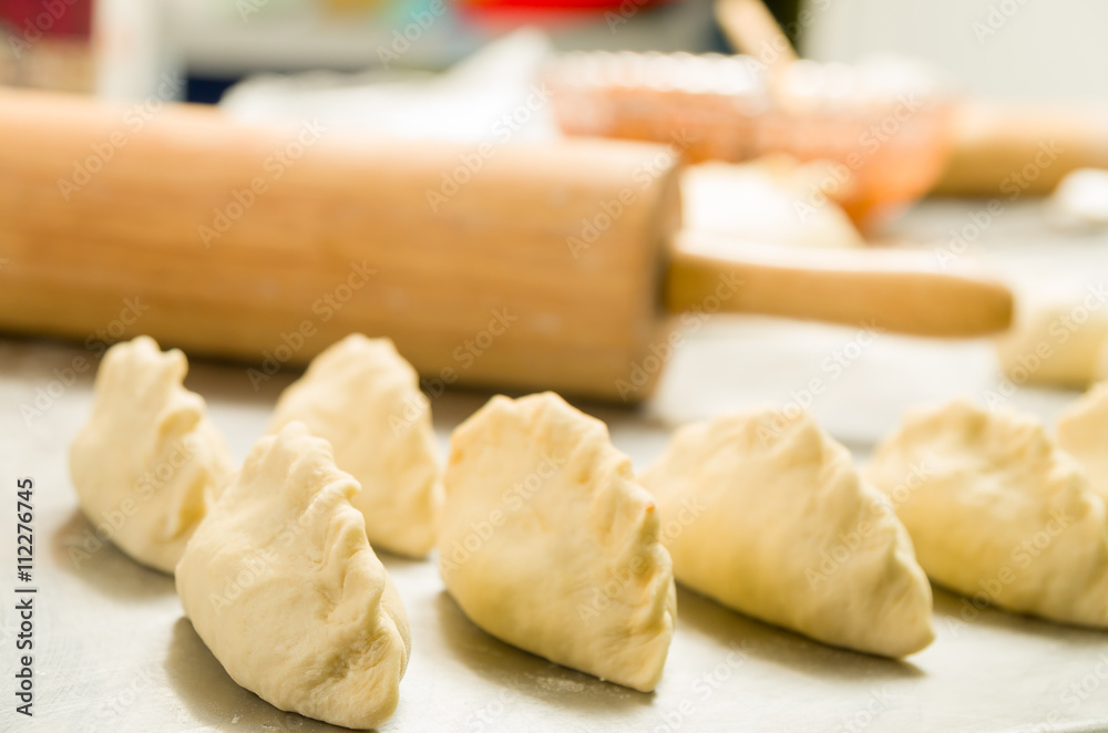 Closeup small delicious empanadas lined up before baking, rolling pin background