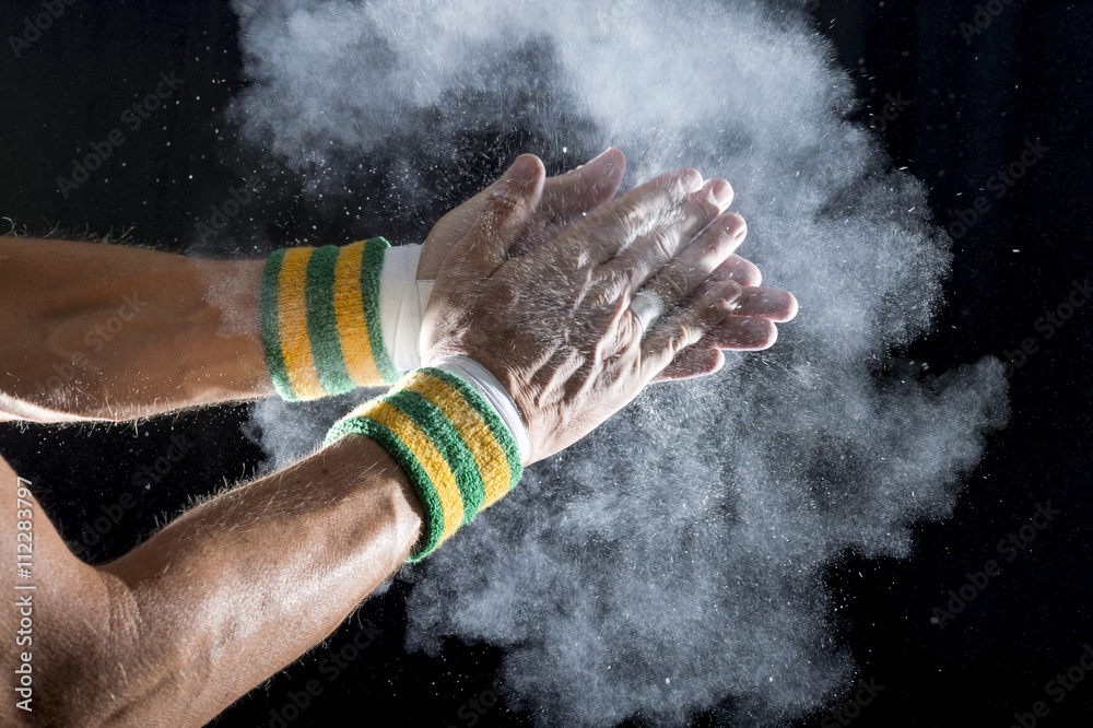 Taped hands of gymnast wearing Brazil colors wristbands clapping white chalk powder into a cloud against dark background