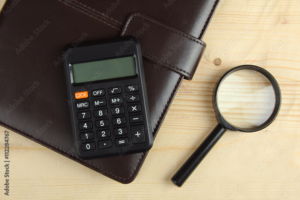 notebook on a brown wooden background with a calculator and magnifying glass notebook on a brown wooden background with a calculator and magnifying glass