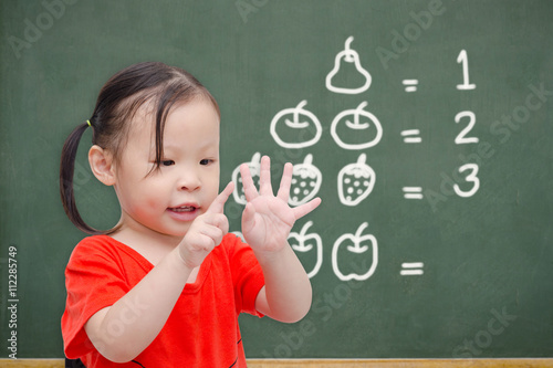 Little asian girl counting her finger in font of chalkboard photo