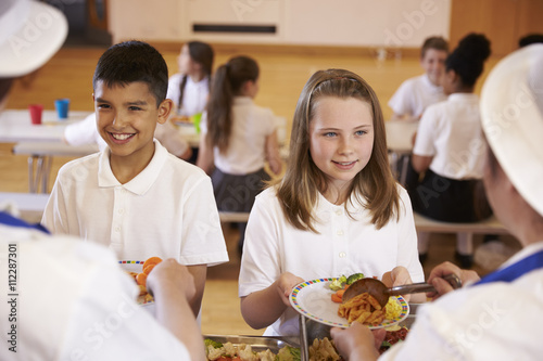 Over shoulder view of kids being served in school cafeteria photo