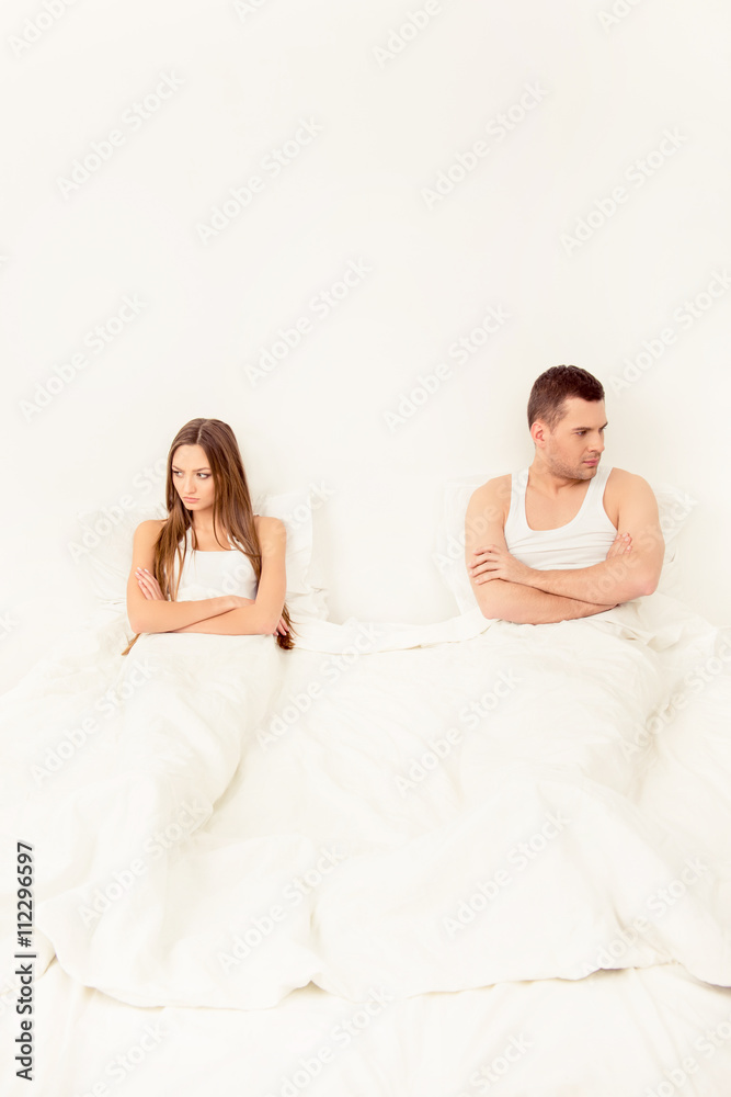 Young depressed couple sitting in bed after quarrel Young depressed couple sitting in bed after quarrel