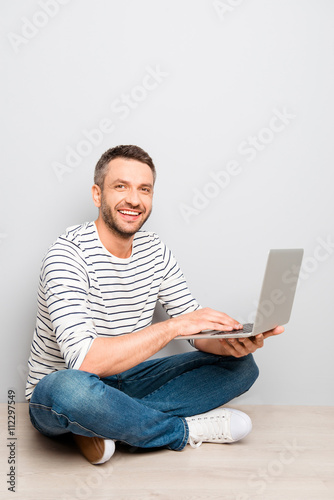 Cheerful happy smiling man sitting on floor with laptop