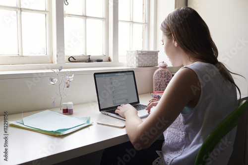 Teenage Girl Studying In Bedroom Using Laptop photo