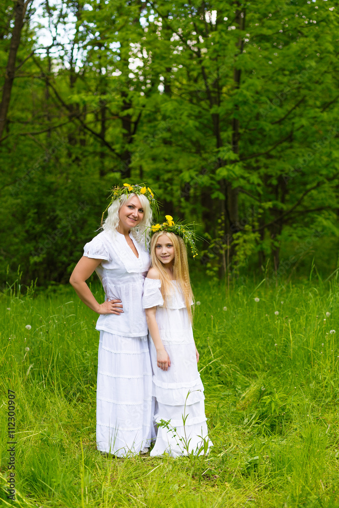 Beautiful and happy mum and daughter with wreaths on the head outdoors in the summer Beautiful and happy mum and daughter with wreaths on the head outdoors in the summer