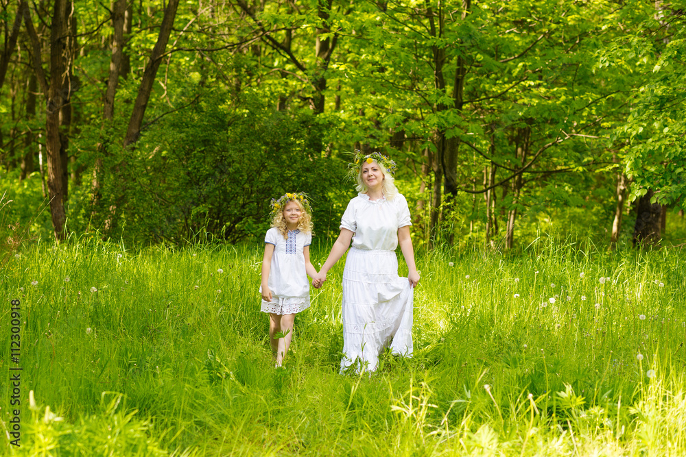 Beautiful family goes hand in hand. Happy family resting on the nature in the summer. Mom and daughter with wreath in the flowers in the park Beautiful family goes hand in hand. Happy family resting on the nature in the summer. Mom and daughter with wreath in the flowers in the park