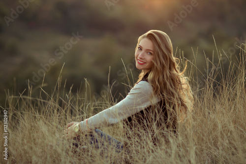 Happy,cheerful,joyful,smiling girl sitting on the hill with very incredibly,beautiful view,watch sunset.Beautiful girl sitting outdoor,in mountains,sunlight,sunny field.Attractive girl with nice smile