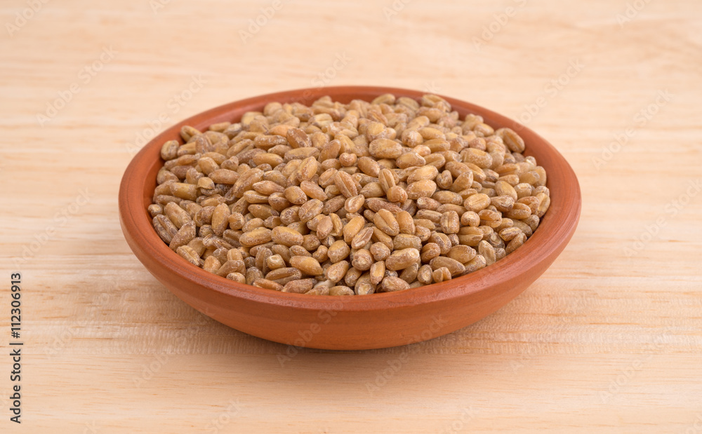 Small bowl of red winter wheat berries on wood table Small bowl of red winter wheat berries on wood table