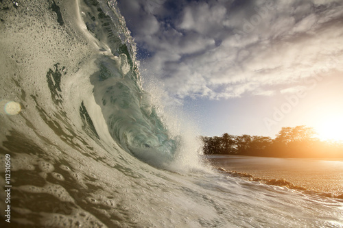 Close up of splashes of a curly turquoise stormy wave crashing at a sandy tropical beach